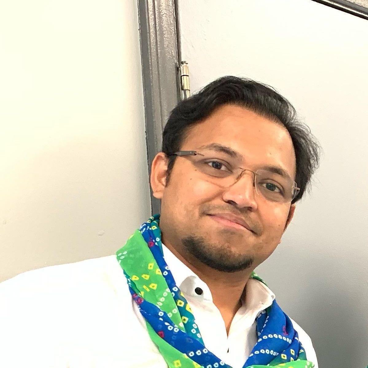 A man wearing glasses and a scarf around his neck is smiling for the camera.