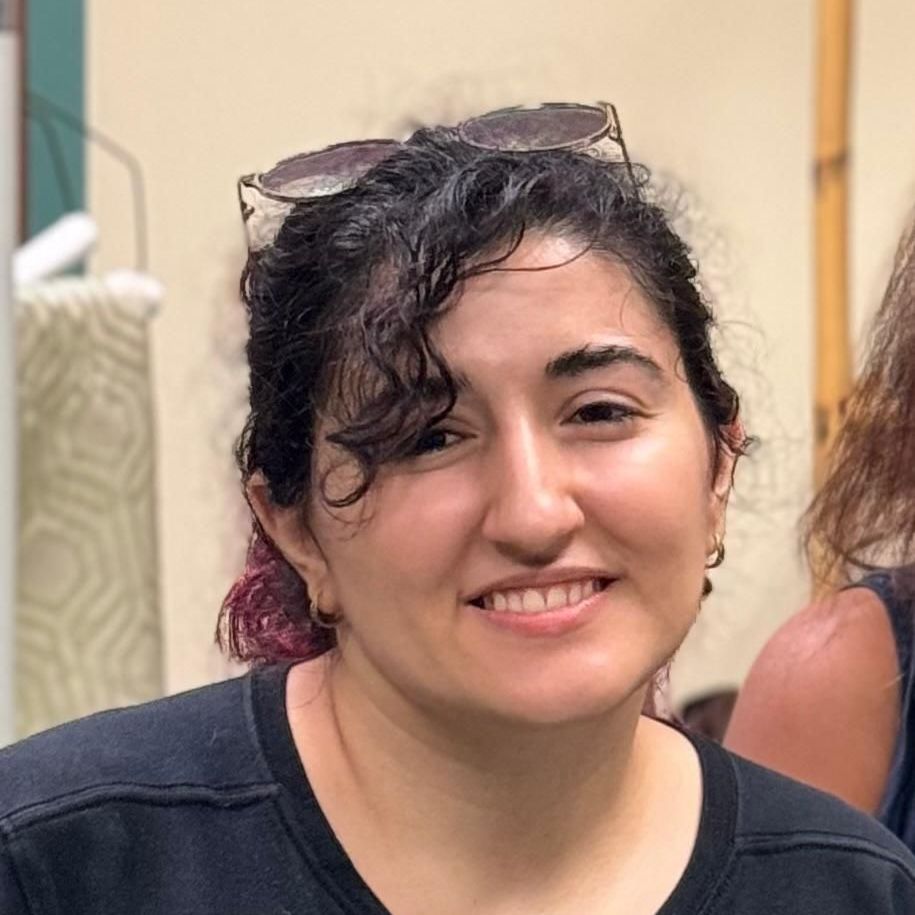 A woman wearing sunglasses and a black shirt is smiling for the camera.