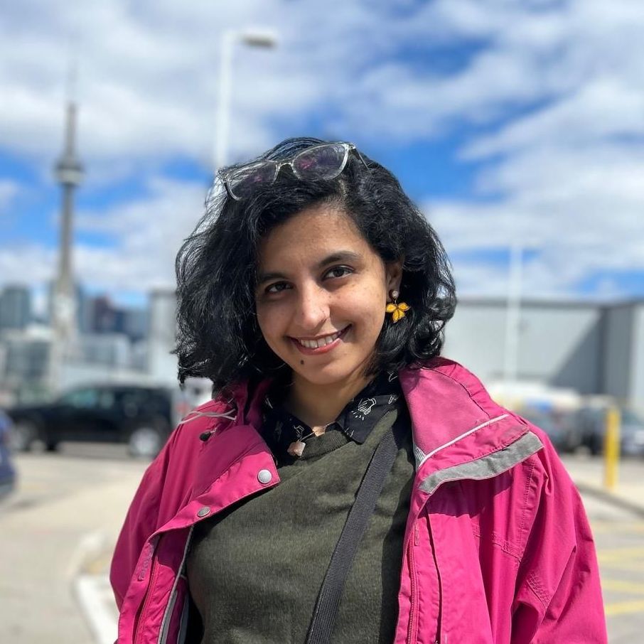 A woman wearing a pink jacket and sunglasses is smiling for the camera.