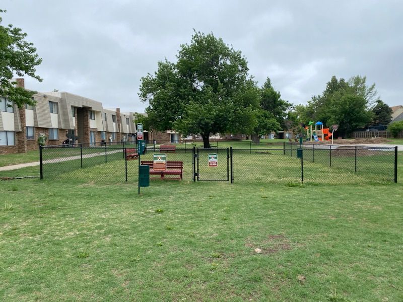 a fenced in dog park with a playground in the background
