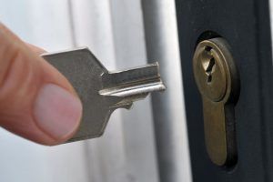 A person is holding a key in front of a door lock.