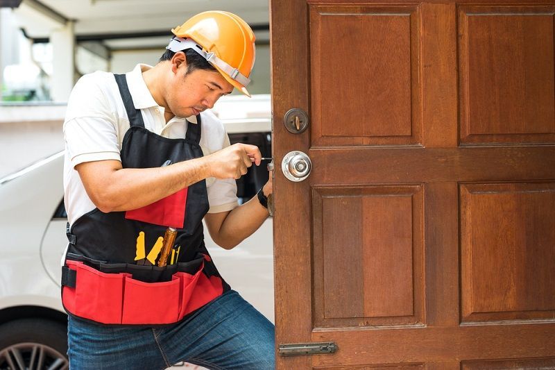 A man in a hard hat is fixing a door lock.