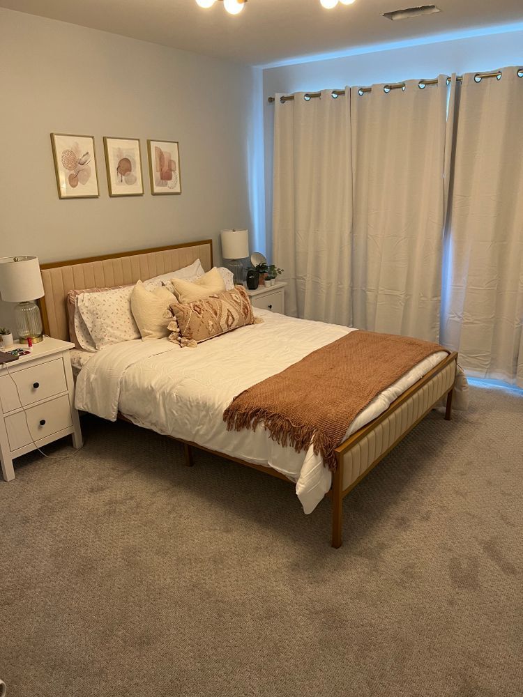 A bedroom with a bed , nightstand , lamps and curtains.