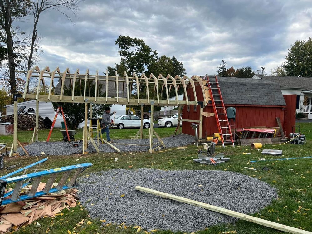 A wooden structure is being built in a yard in front of a red barn.