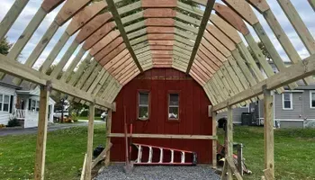 A red barn is under construction with a ladder in front of it.