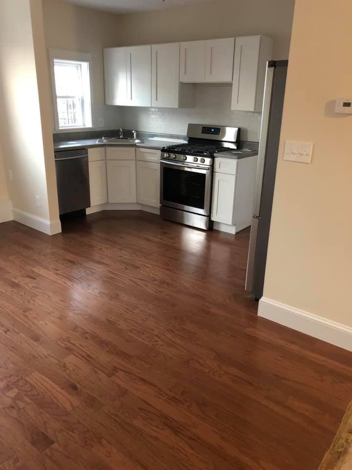 An empty kitchen with hardwood floors and white cabinets.