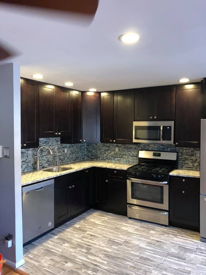 A kitchen with black cabinets , stainless steel appliances , a sink , stove , microwave and refrigerator.