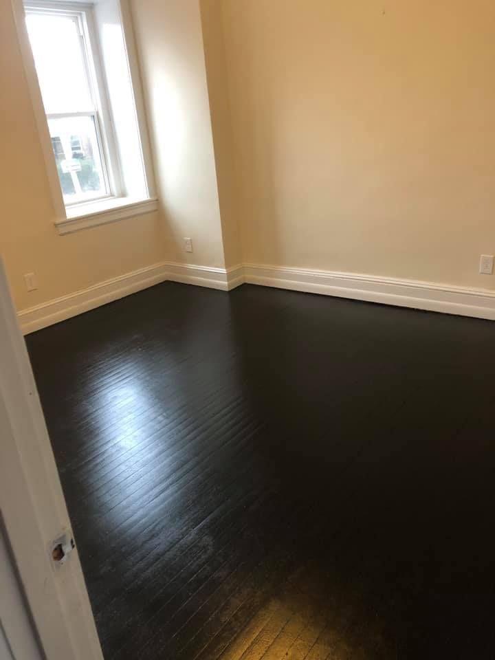An empty room with a black wooden floor and a window.
