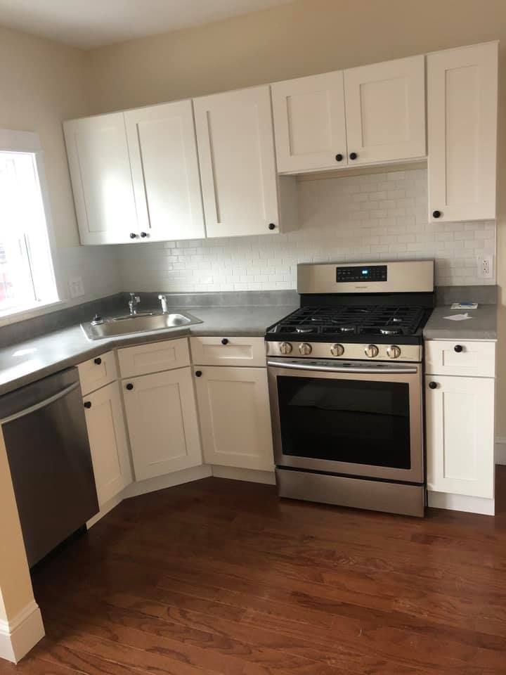 A kitchen with white cabinets , a stove , a sink and a dishwasher.