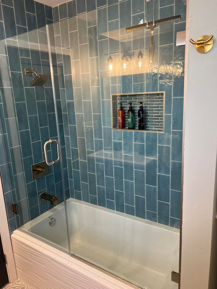A bathroom with blue tiles and a bathtub with a glass shower door.