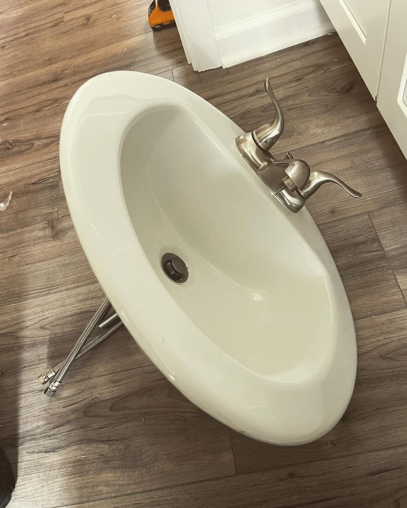A white sink is sitting on a wooden floor in a bathroom.
