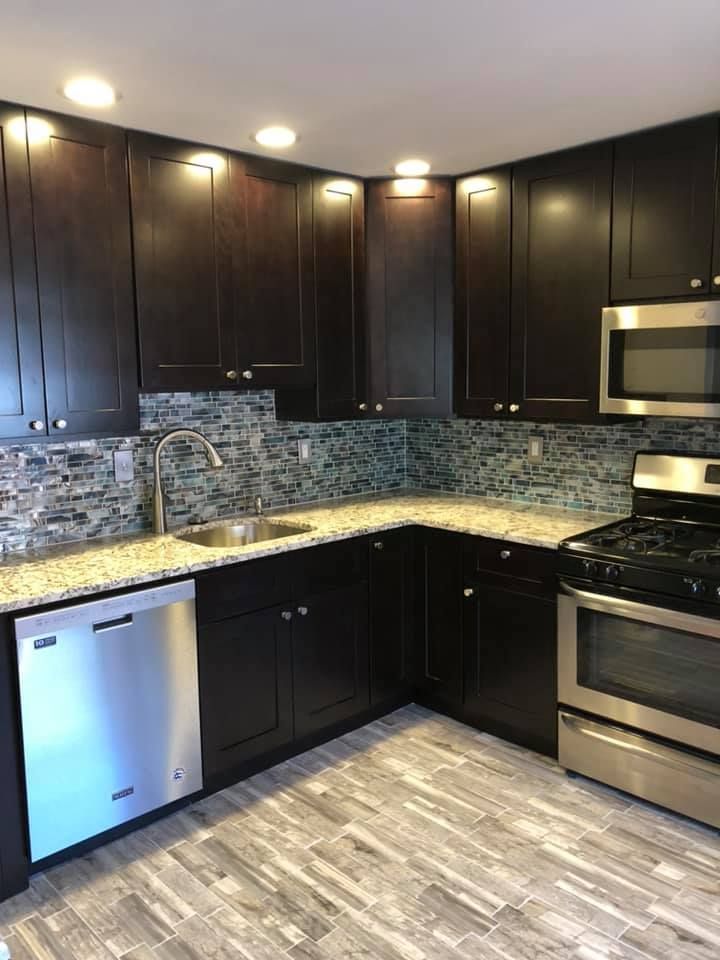 A kitchen with black cabinets , stainless steel appliances , a sink , and a stove.