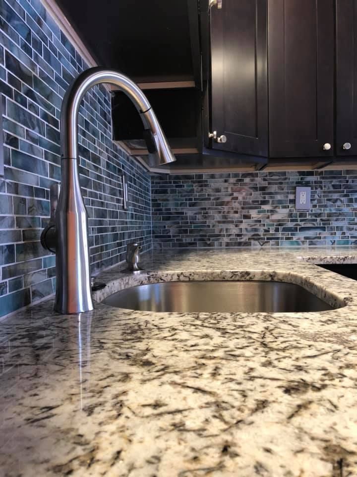 A kitchen sink with a stainless steel faucet on a granite counter top.