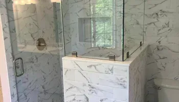 A bathroom with marble tiles and a walk in shower with a glass door.