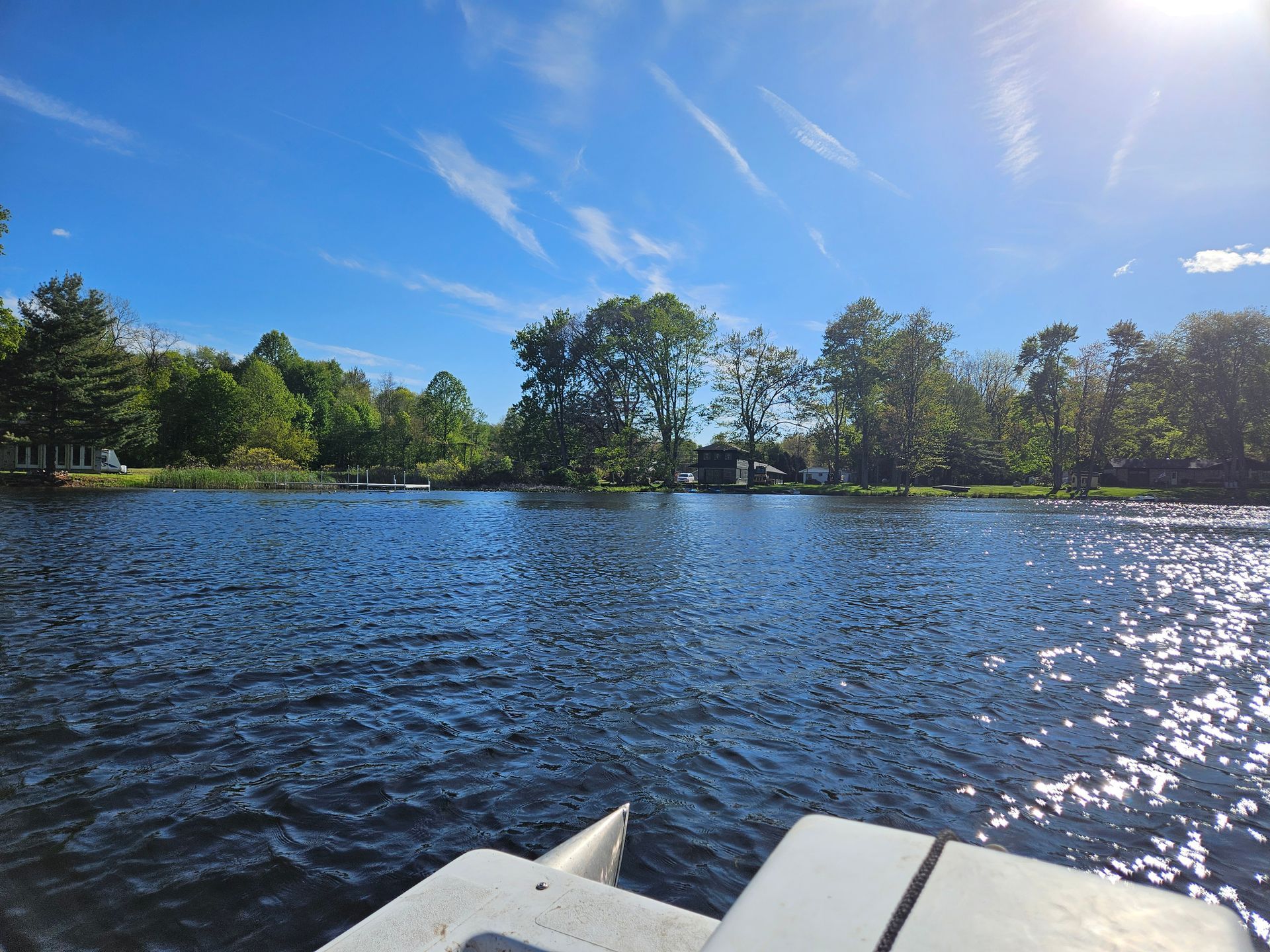 View from a boat on a sunny lake with trees along the shoreline and blue sky above