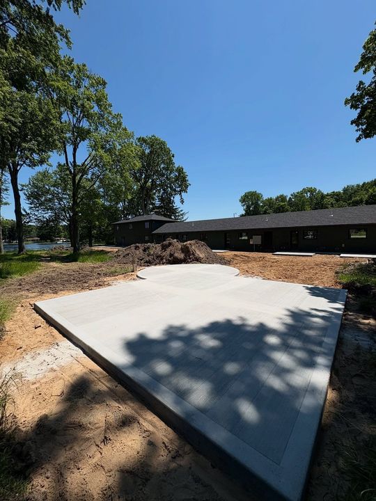 Concrete slab in a wooded yard beside a low building under a clear blue sky