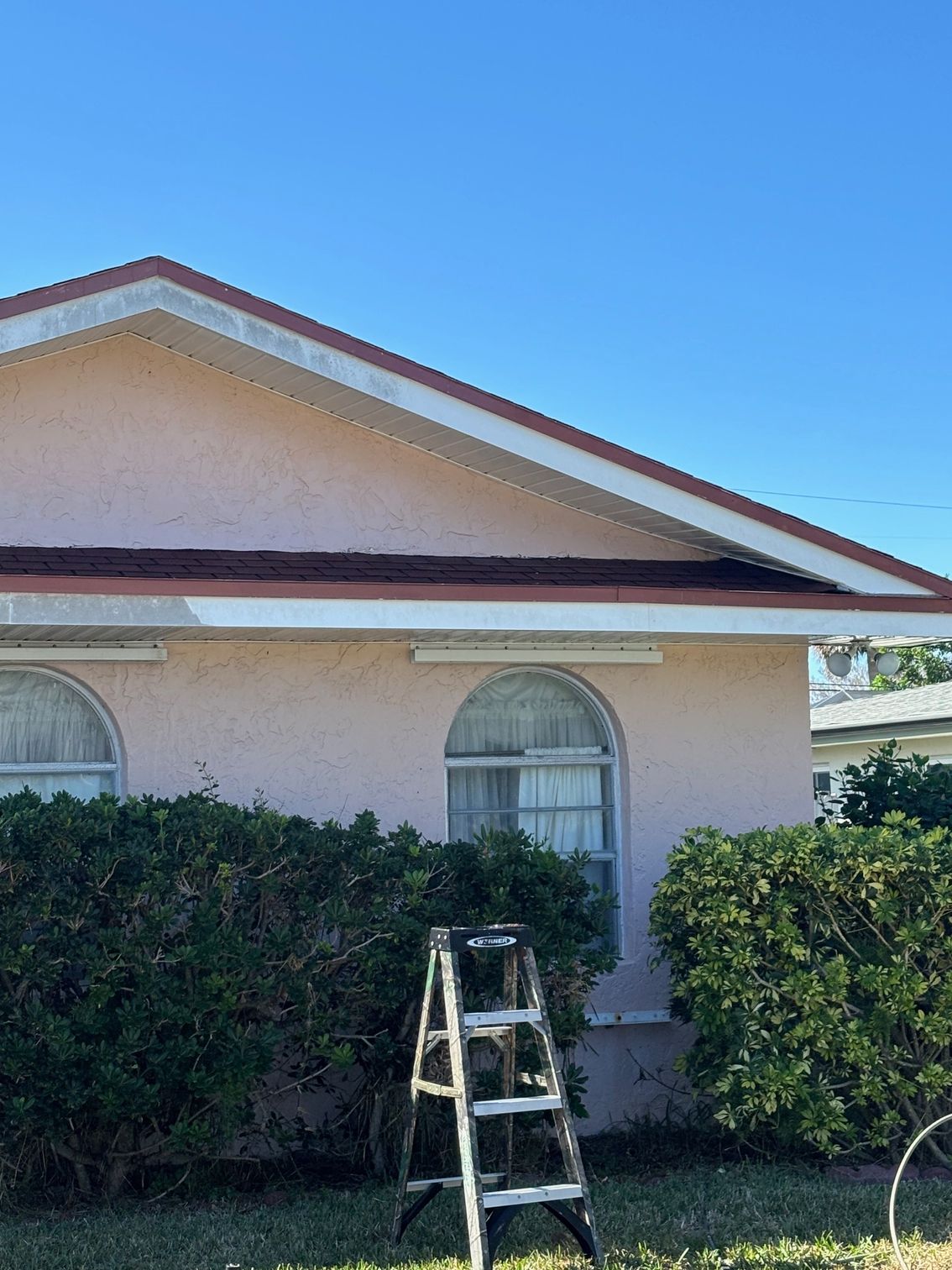 A ladder is sitting in front of a pink house.