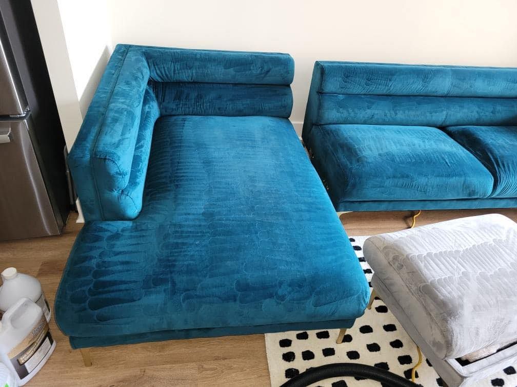 Teal chaise lounge and sofa with gold legs, next to a carpet cleaner and a black and white patterned rug.