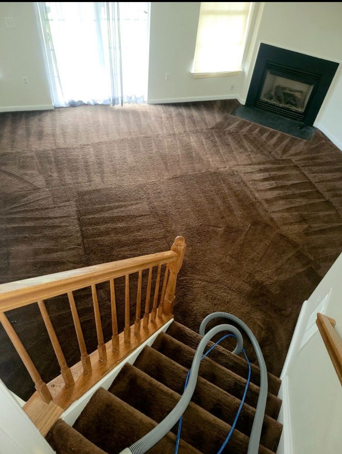 Brown carpeted stairs leading to a living room with a fireplace, cleaned with a vacuum.