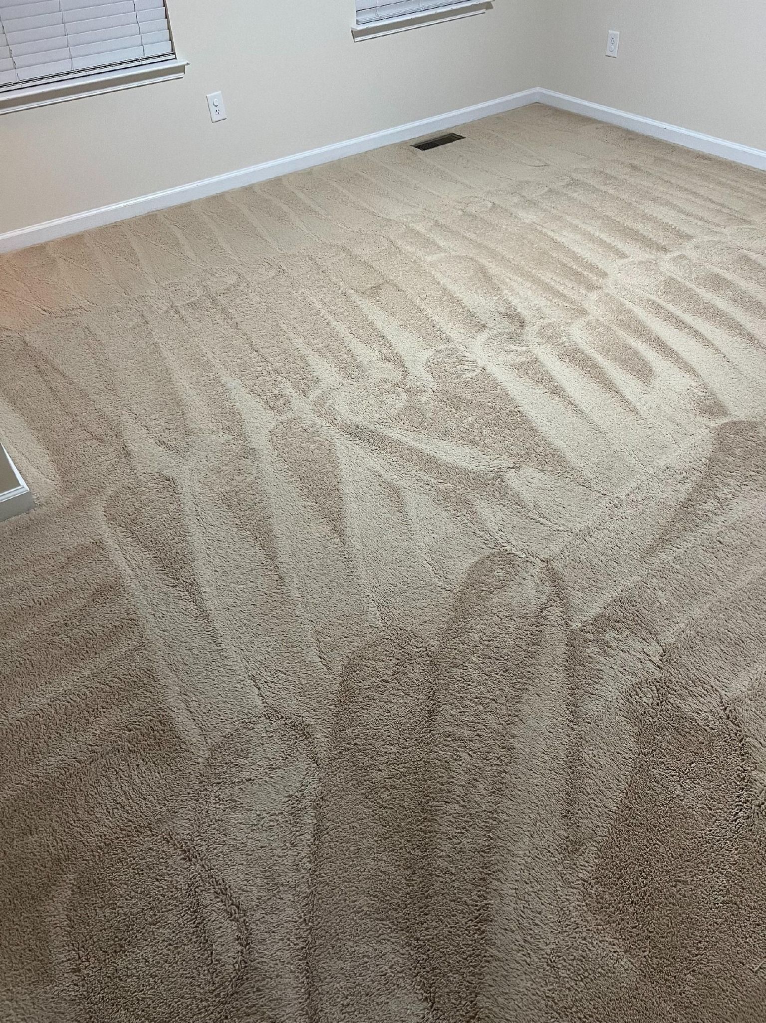 Beige carpeted room, with light-colored walls. Visible vent and window trim.