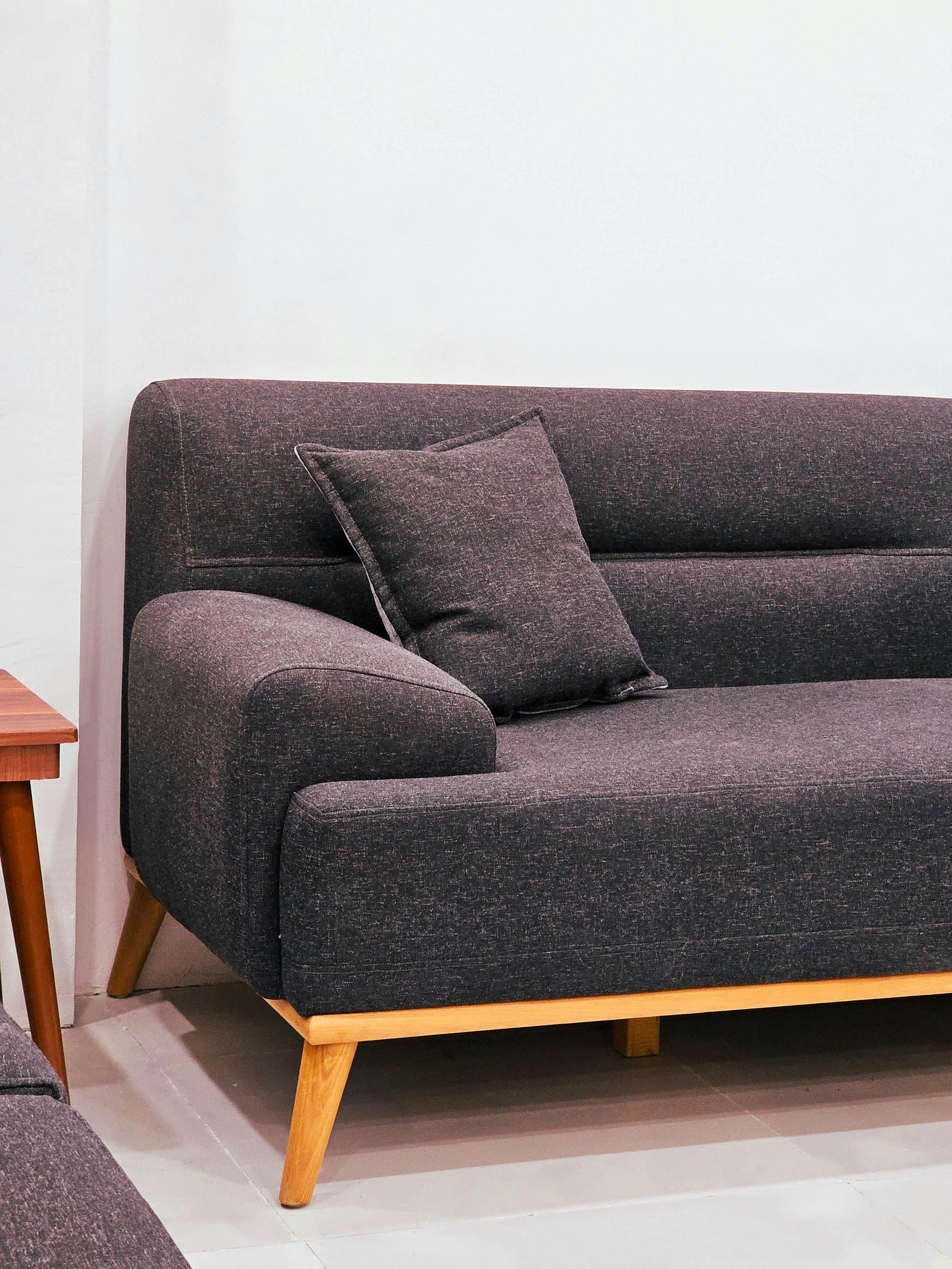 Dark gray tweed sofa with light wood legs and one pillow against a white wall.