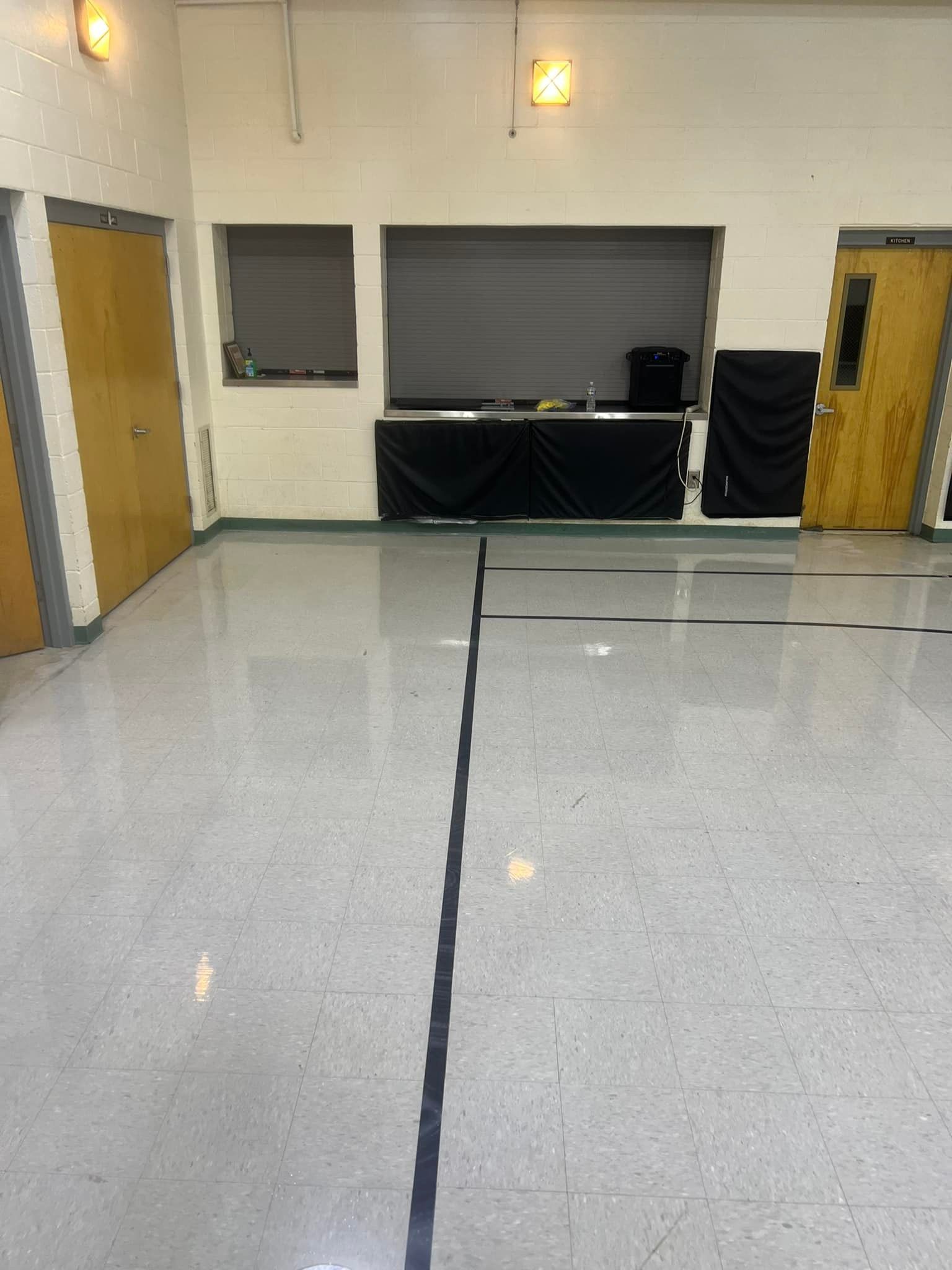 A room with a shiny gray floor and a black line down the center. There are doors and a counter in the background.