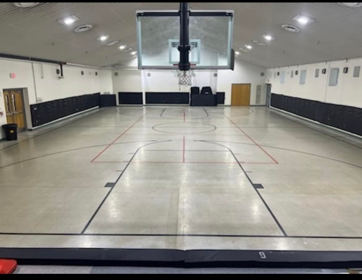 Empty indoor basketball court with black padding, and red/black court lines.
