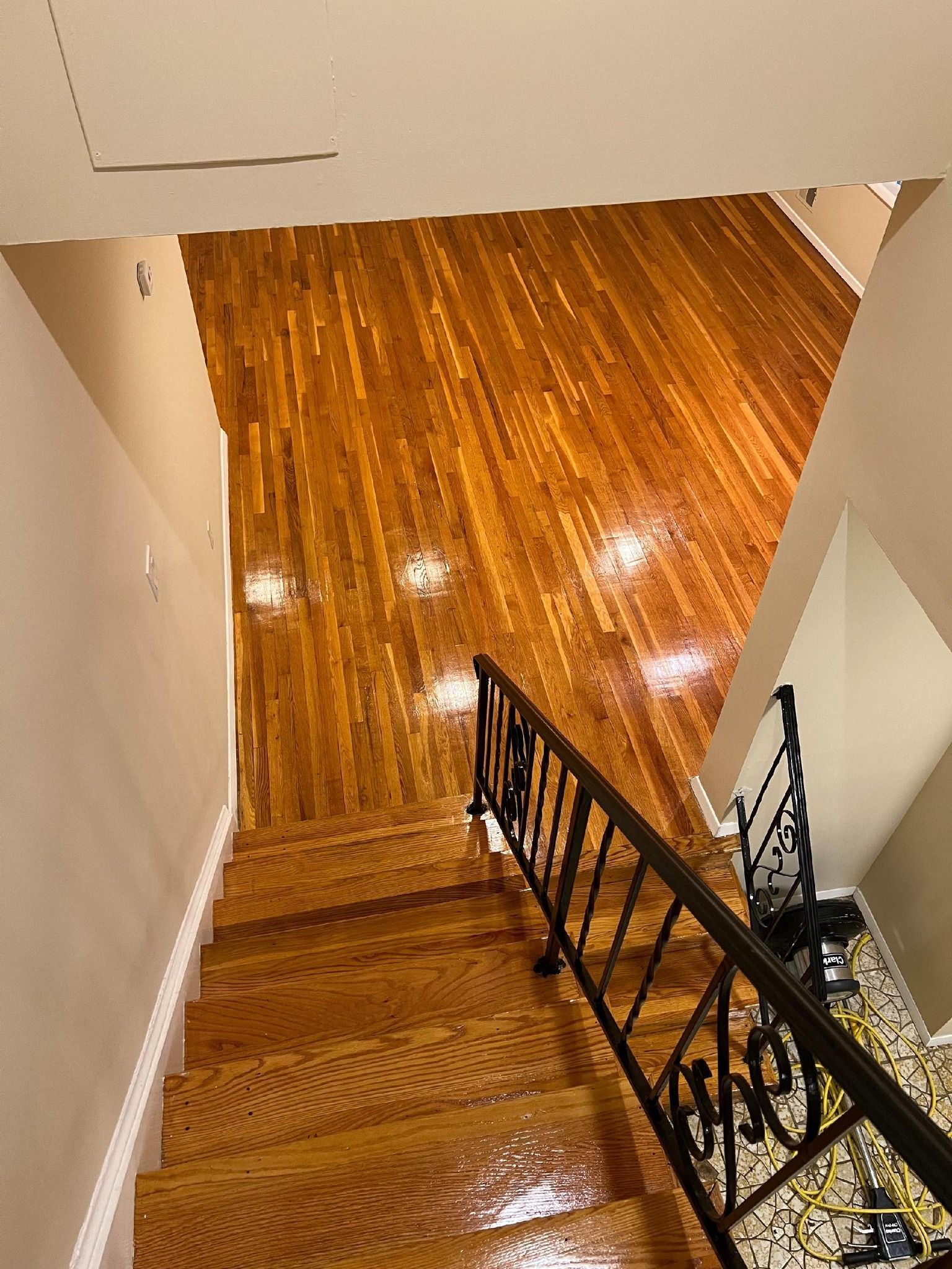 Wooden stairs leading up to a hardwood floor; a black handrail runs along the right.