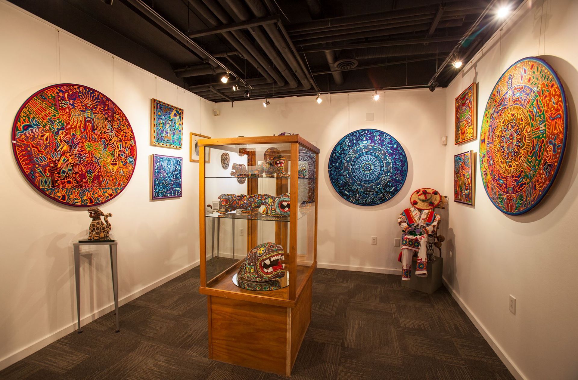 A dining room with a glass table, white chairs, a modern chandelier, and three framed abstract art pieces on the wall.