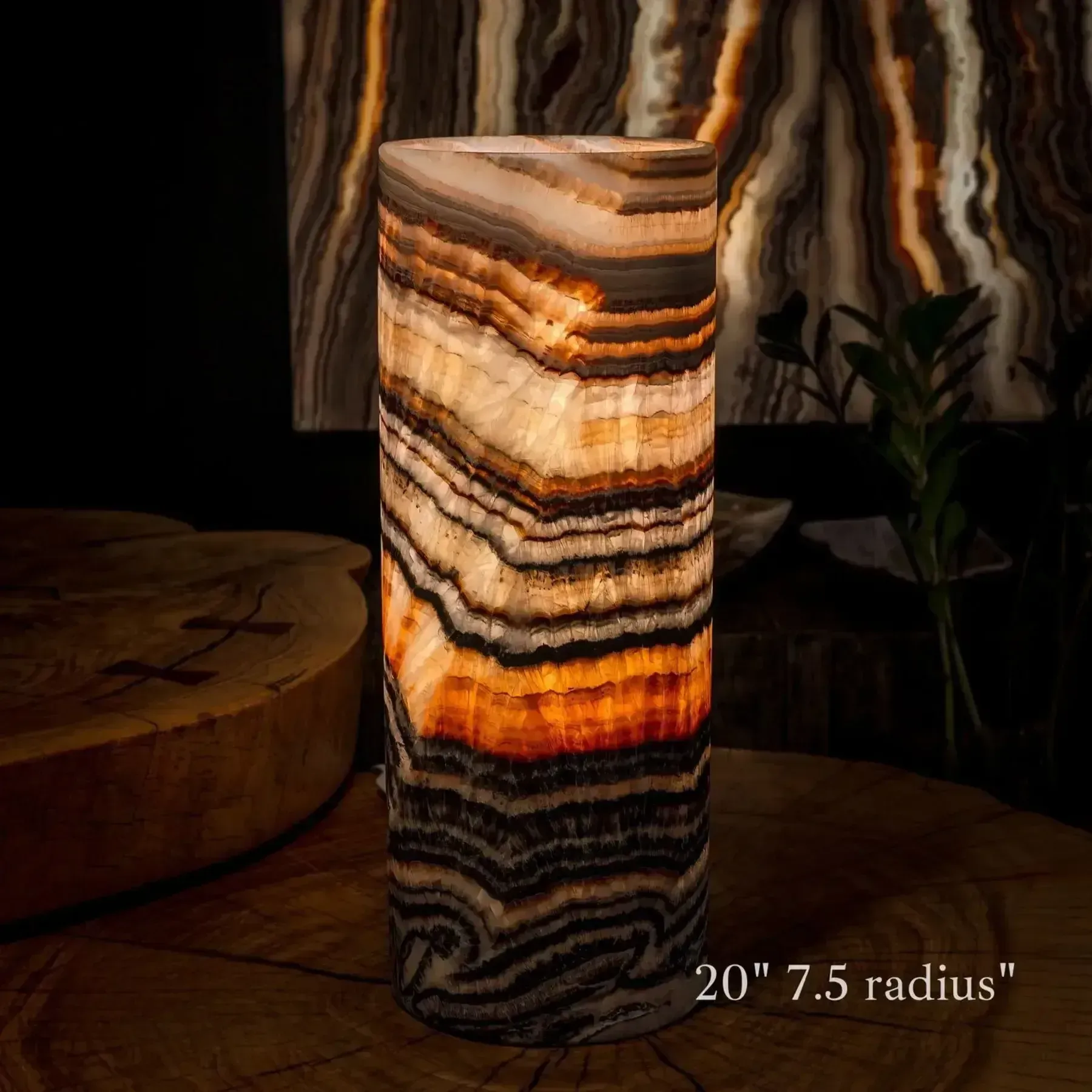 A cylindrical, lit onyx stone lamp with horizontal, earthy-toned bands rests on a dark wooden table.