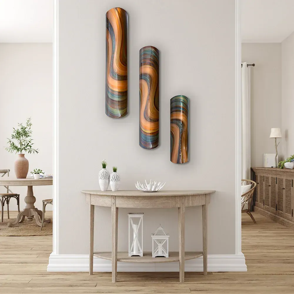 Three vertical, curved metal wall art pieces in shades of copper, blue, and black, hanging above a half-moon wooden console.