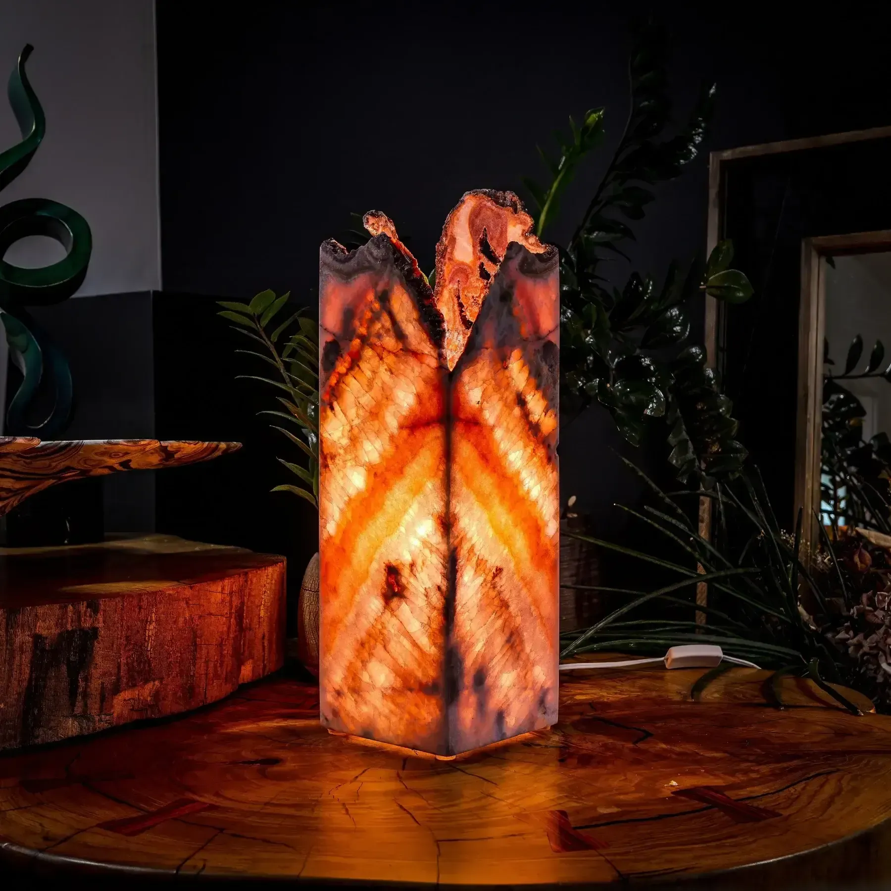 A glowing, cylindrical lamp made of translucent amber and orange agate stone sits on a wooden table in a dimly lit room.