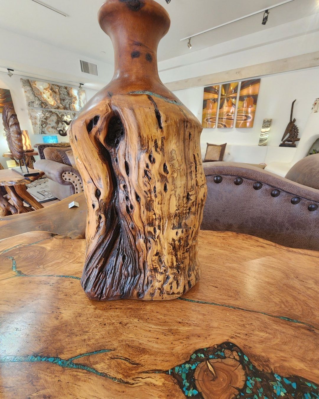 A handcrafted, rustic wooden vase with a textured, burl-like surface sitting on a table with turquoise inlay details.