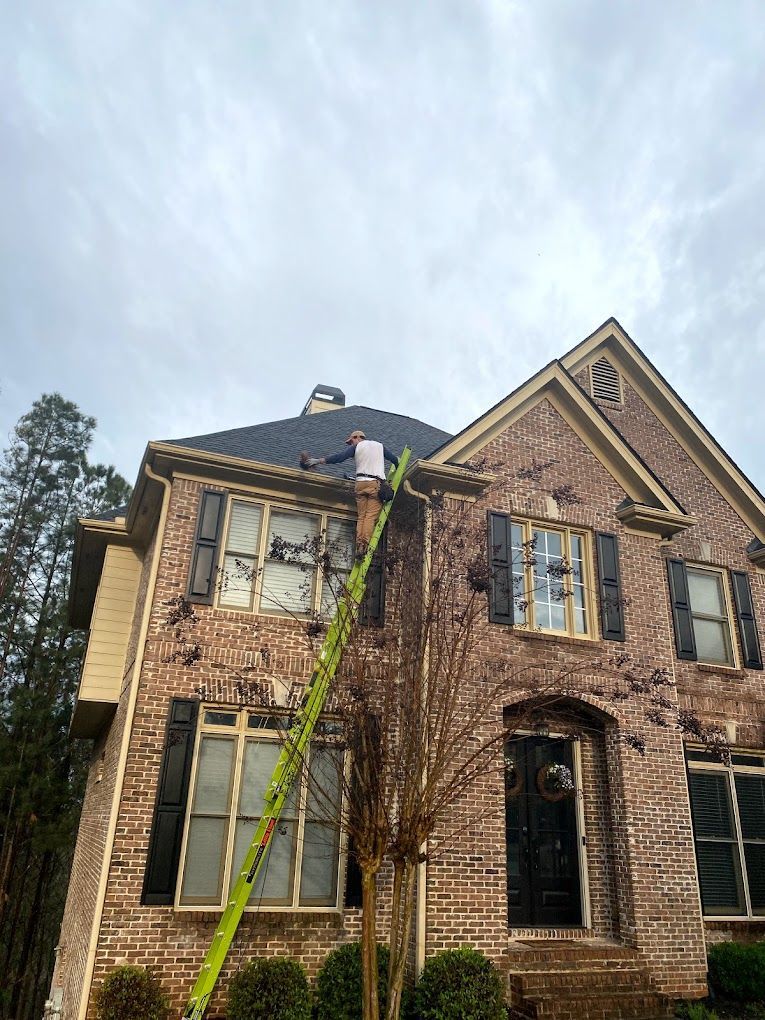 wildlife removal near me Person on a tall ladder cleaning gutters on a brick house under a cloudy sky.
