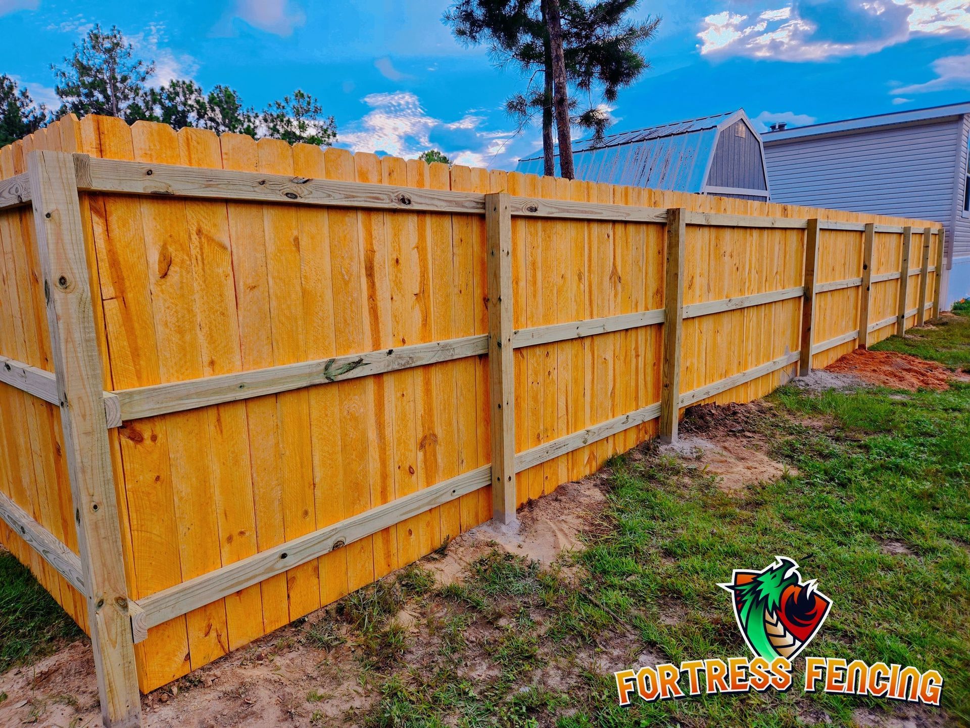 Wooden fence in a yard, stained light brown, with green grass and a blue sky.