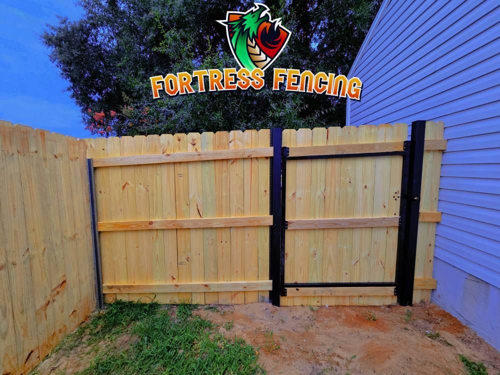 Wooden fence with black gate and Fortress Fencing logo.