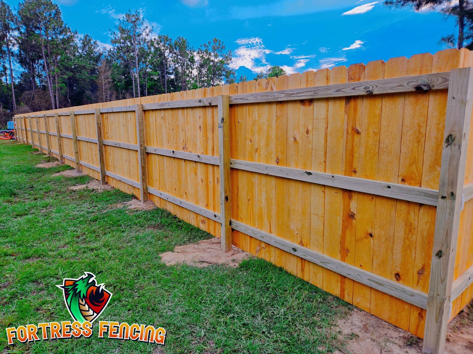 Wooden privacy fence in a grassy yard under a blue sky.