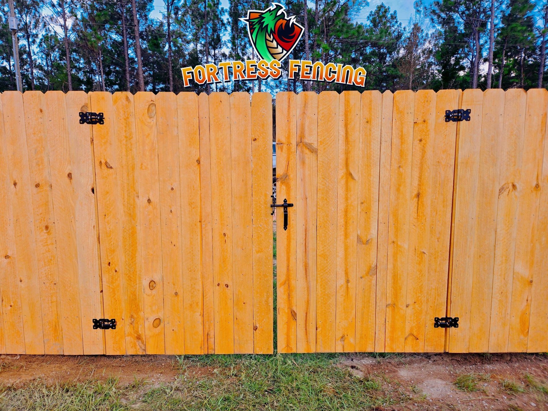 Wooden double gate with black hinges and latch, under a Fortress Fencing sign.