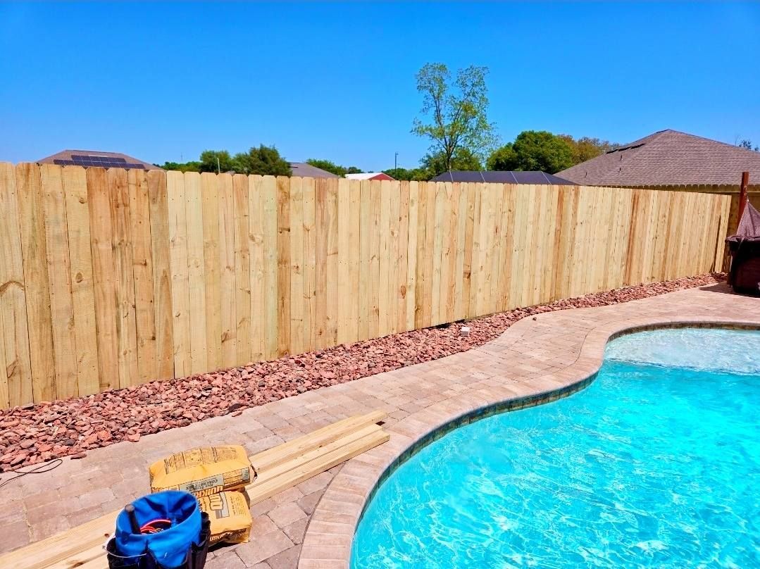 Wooden fence surrounding a backyard pool with clear blue water and clear blue sky.