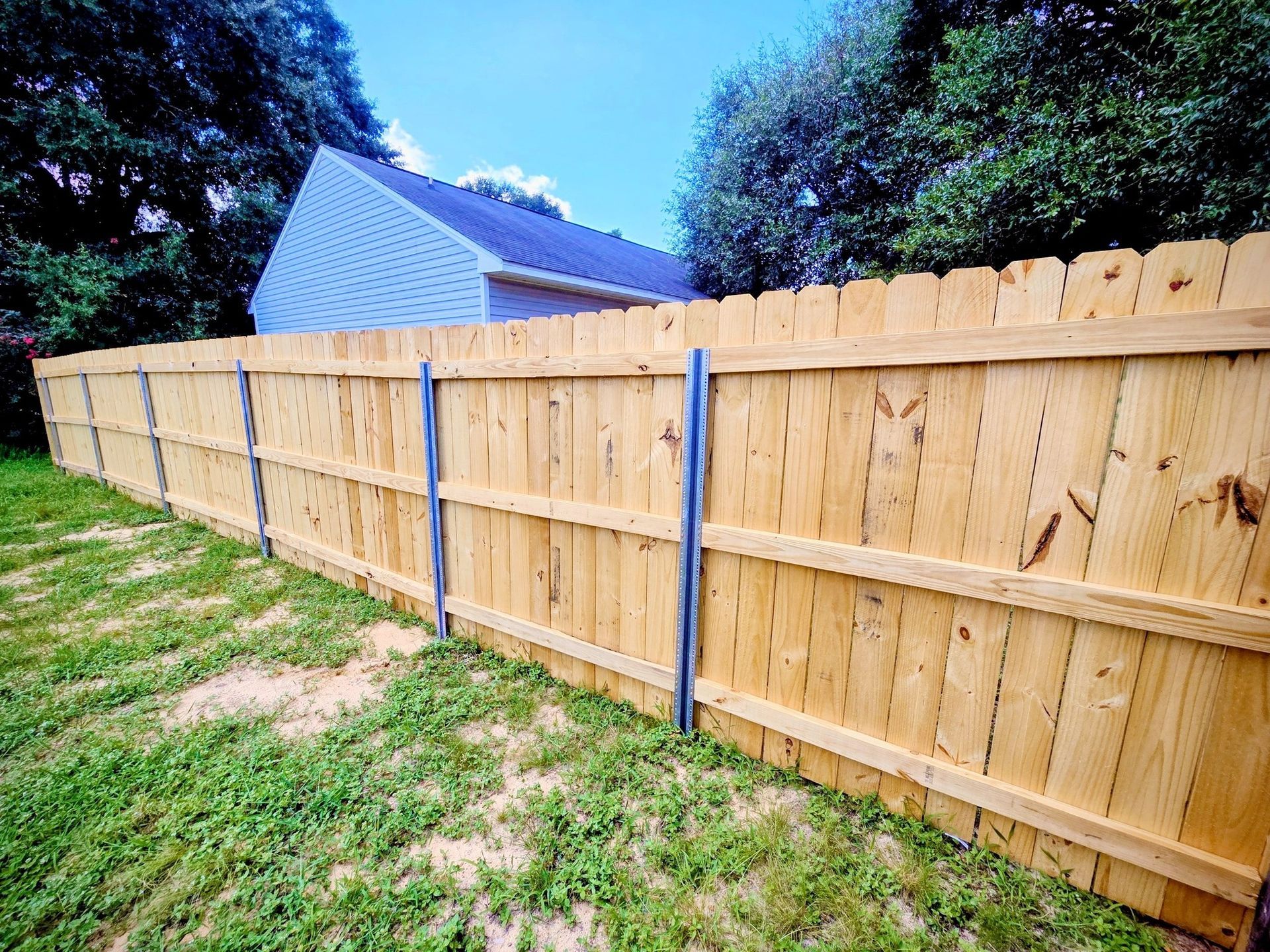 Wooden fence in a grassy yard, with a house and trees in the background.