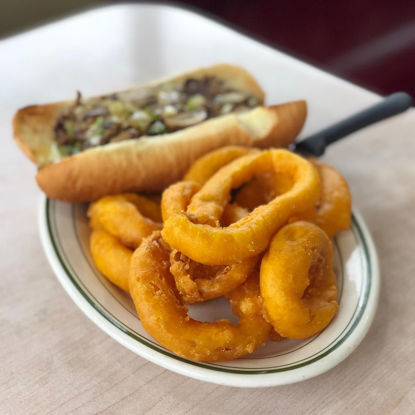 Philly cheesesteak sandwich with onion rings on a plate, diner setting.