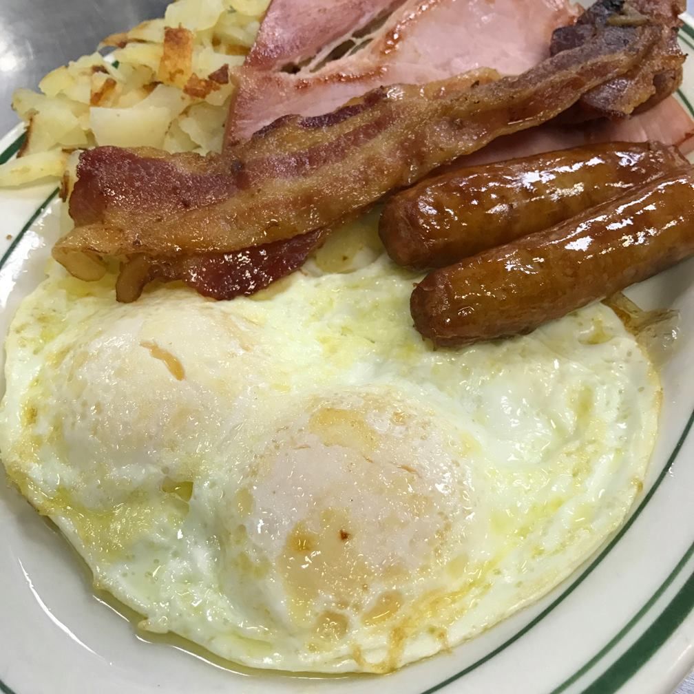 Breakfast plate with fried eggs, bacon, sausage, ham, and potatoes.