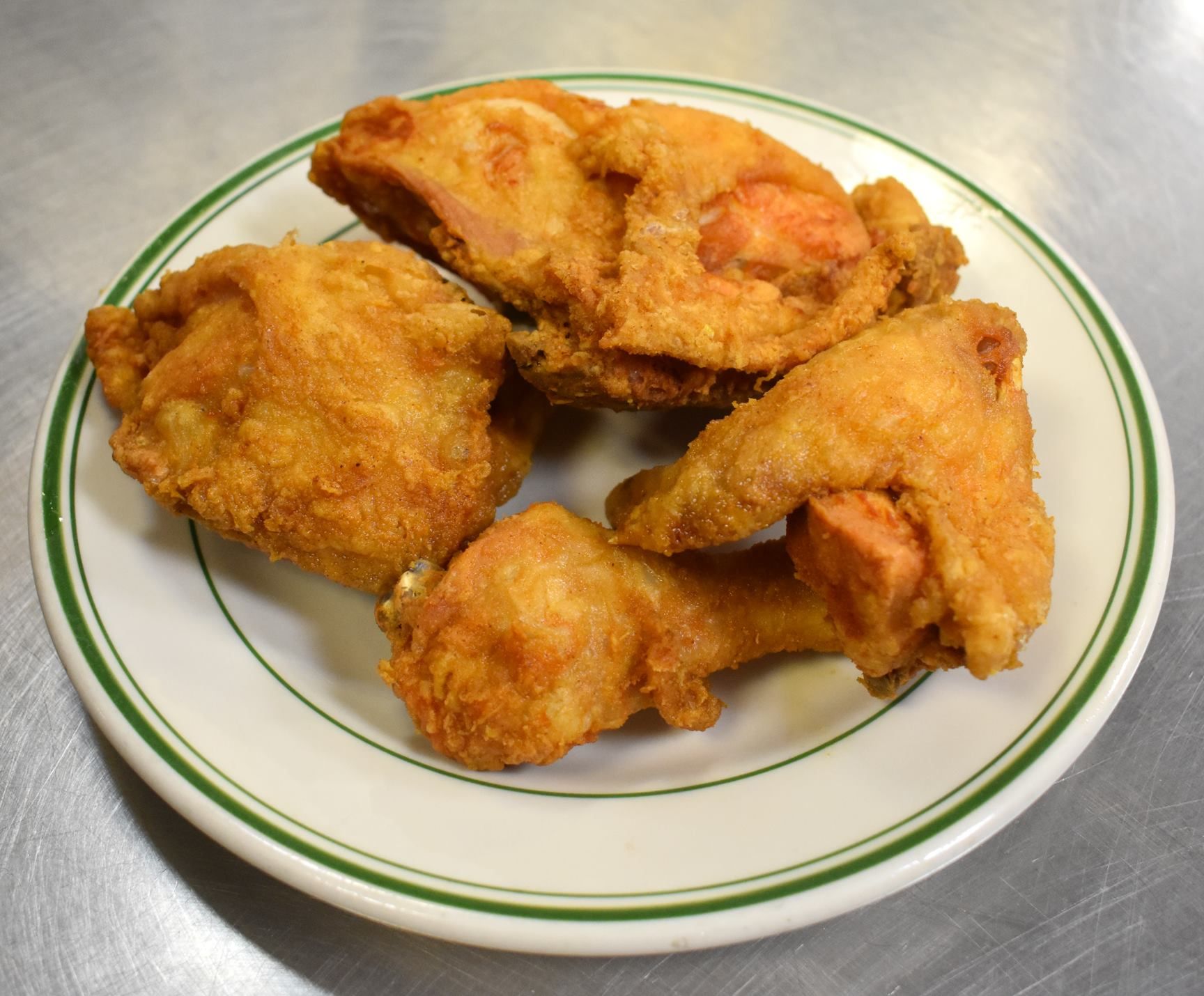 Fried chicken pieces on a white plate with a green rim, on a metallic surface.