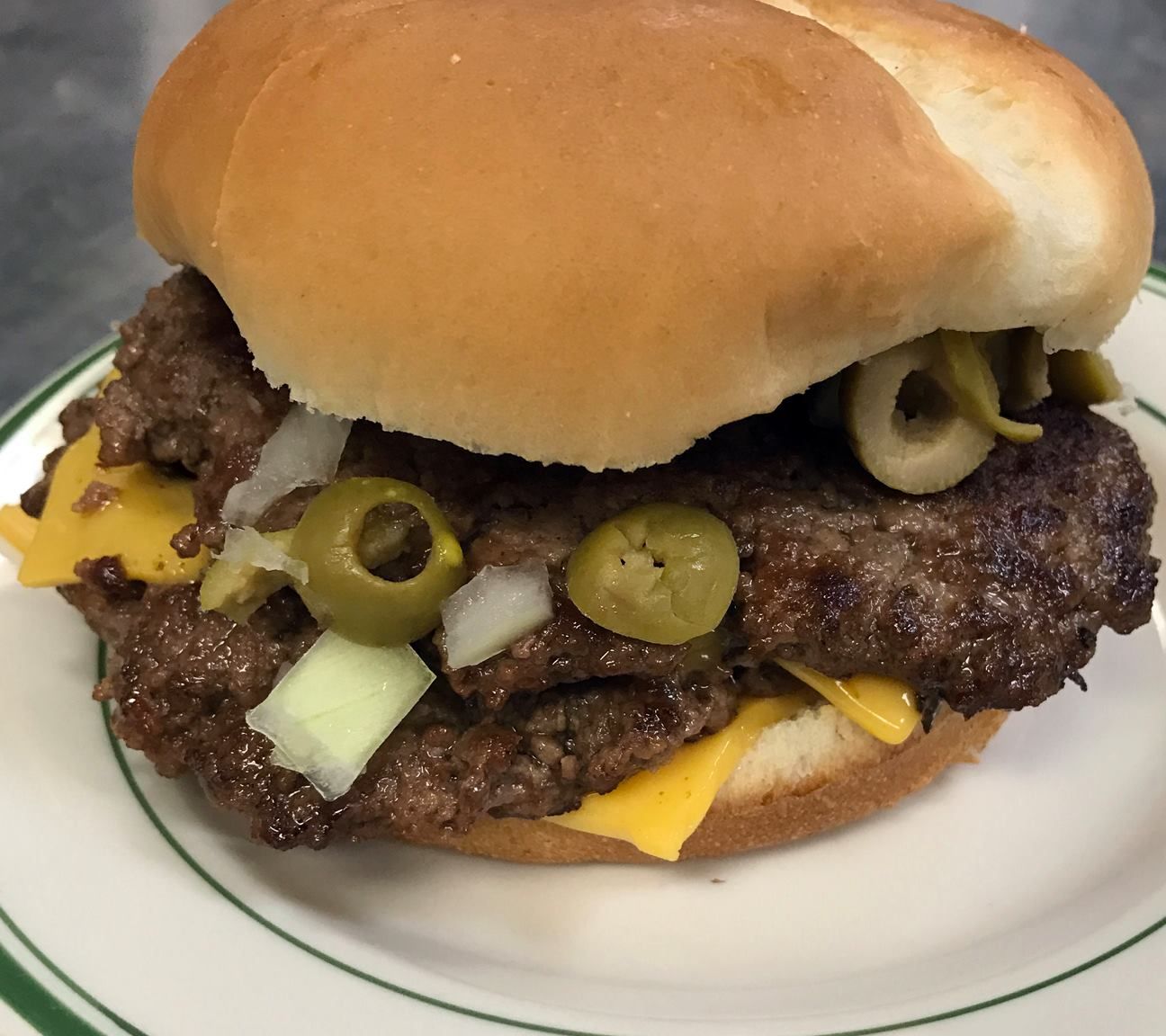 Double cheeseburger with olives and onions on a white plate with a green border.