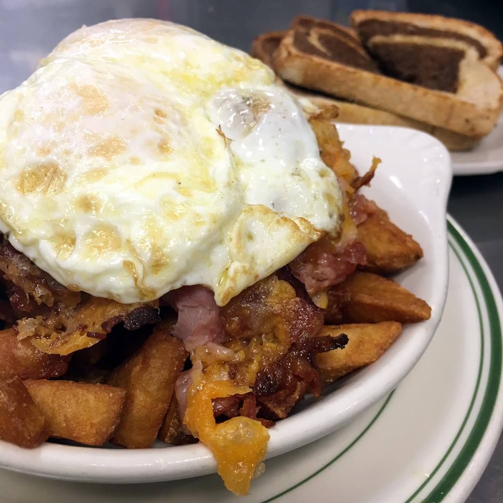 Fried egg over potatoes, bacon, and cheese in a white bowl, with toast on the side.