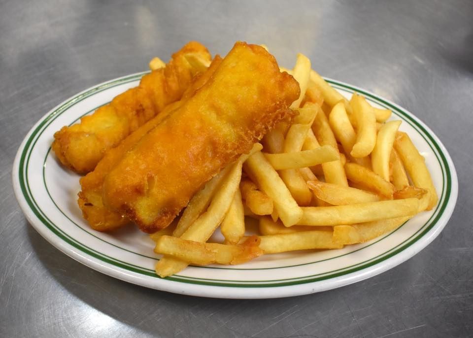 Fish and chips on a white plate with a green rim, on a metal surface.