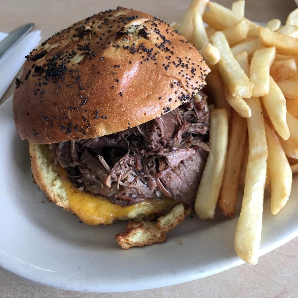 Beef sandwich with cheese on a poppy seed bun, served with fries on a plate.