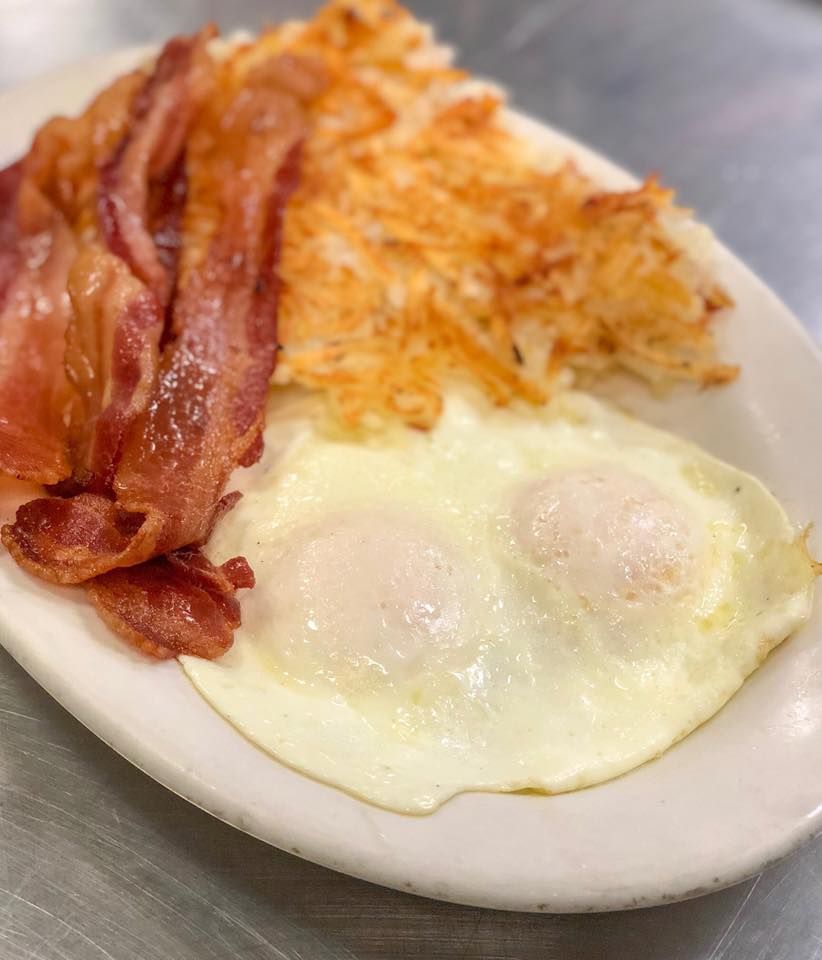 Breakfast plate with bacon, hash browns, and two fried eggs.