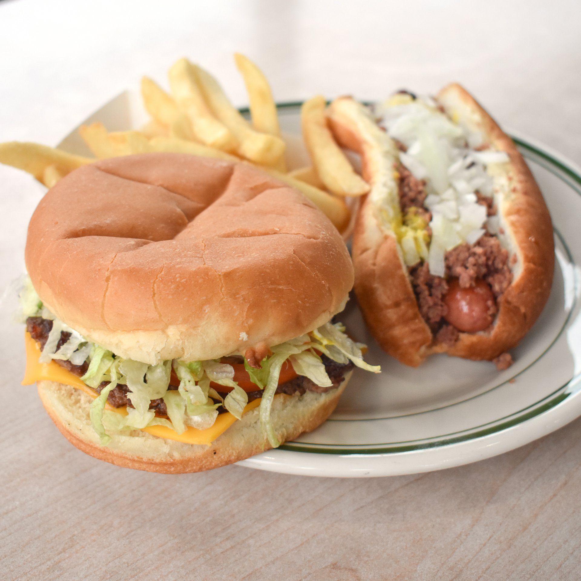 Burger with cheese and lettuce, chili dog with onions, and fries on a plate.