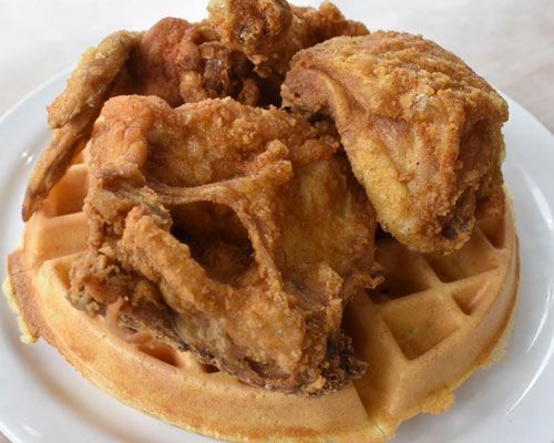 Fried chicken pieces atop a golden waffle on a white plate.
